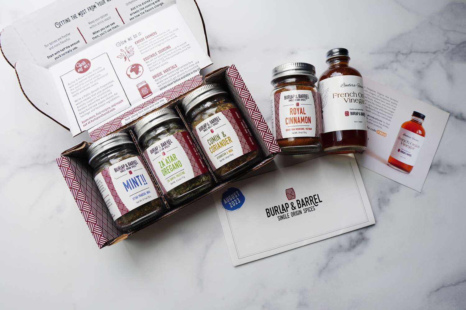 four jars of spices and a small bottle of vinegar on a marble surface