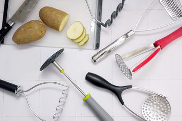 potato mashers on a white backdrop with a sliced potato and cutting board