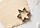 A starshaped cookie cutter on rolled dough sprinkled with flour on a surface