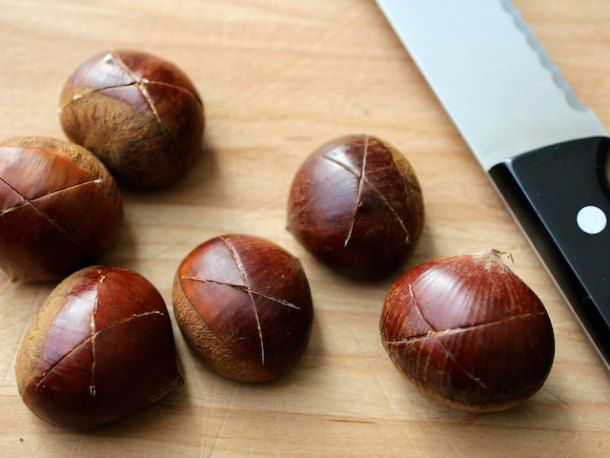 A serrated knife next to six chestnuts with an "X" scored into their skin.