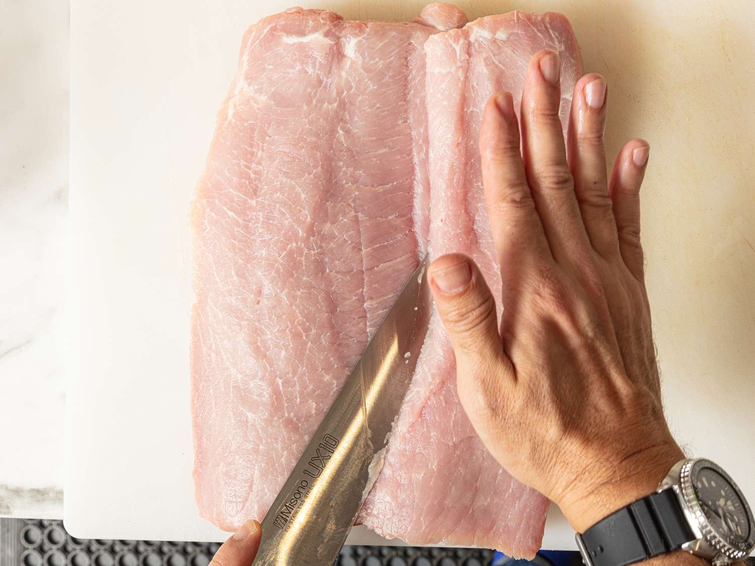 folding over sliced open pork loin with hands and a knife 