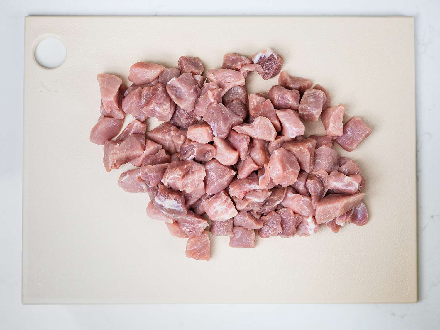 Small chunks of chopped pork shoulder on a plastic cutting board.