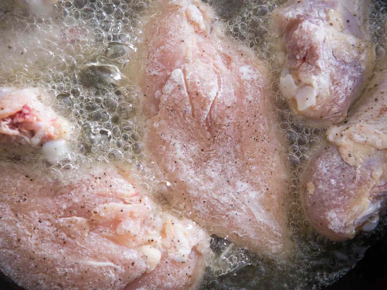 Chicken coated in seasoned flour frying in a cast iron pan.