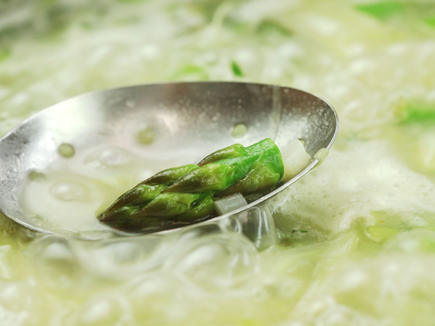 An asparagus tip in a slotted spoon to be transferred out of the stock. 