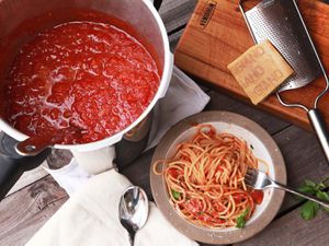 Overhead shot of a pot of pressure cooker tomato sauce, bowl of pasta tossed in tomato sauce, and hunk of parmigiano resting on a cheese grater