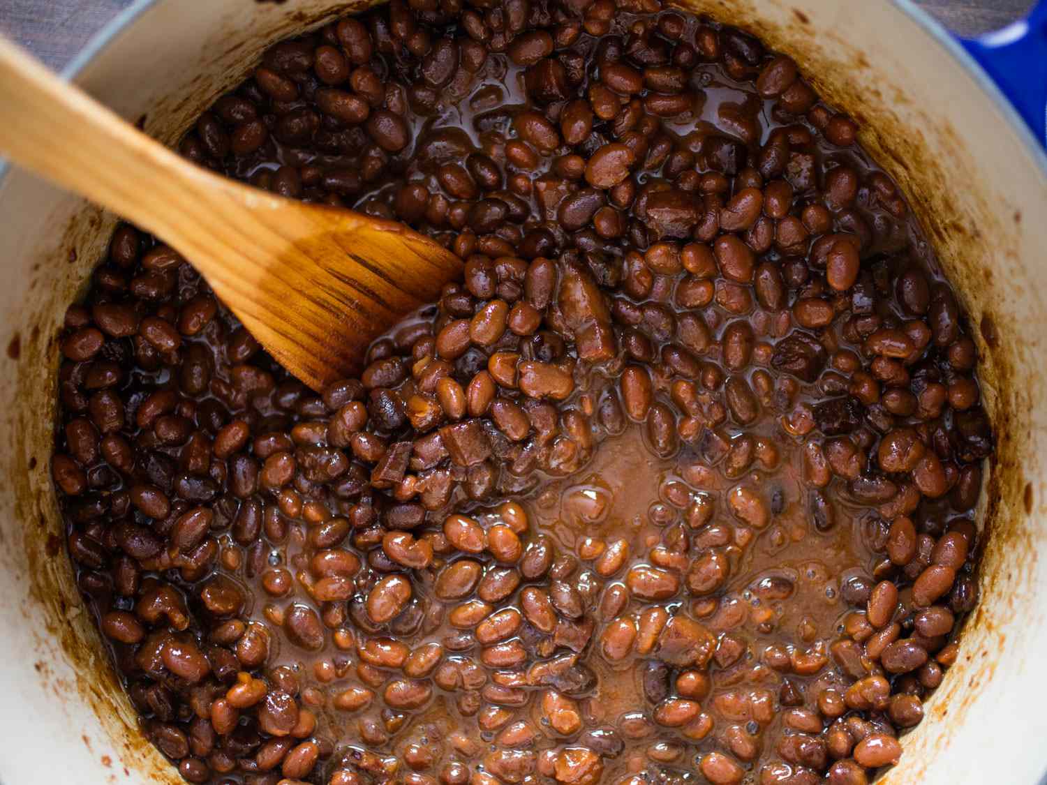 Wooden spoon stirring Dutch oven of baked beans.