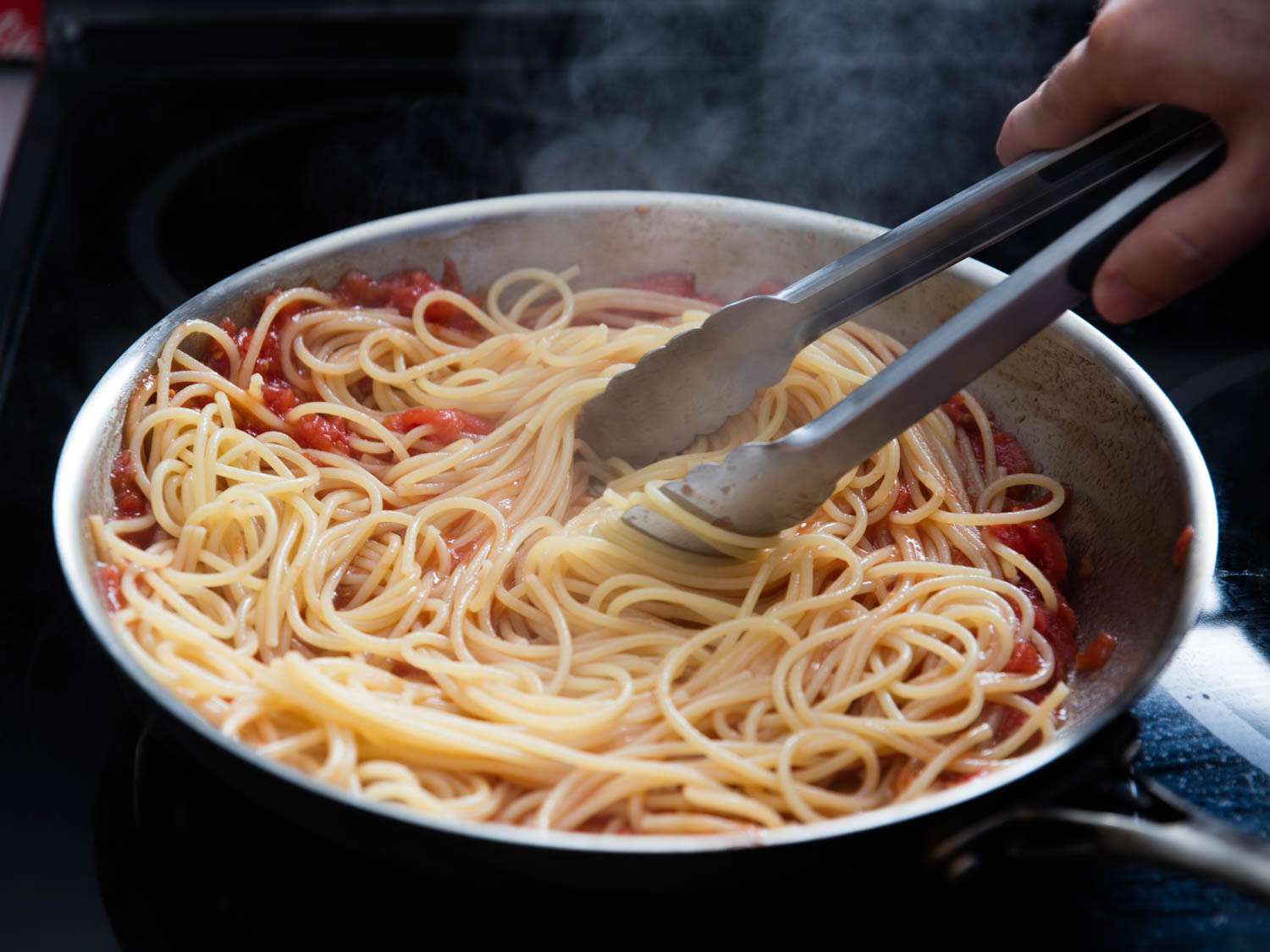 Spaghetti and red pasta sauce being mixed together with a pair of tongs.