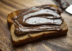 A slice of bread with a generous smear of chocolate hazelnut spread on a wooden board.