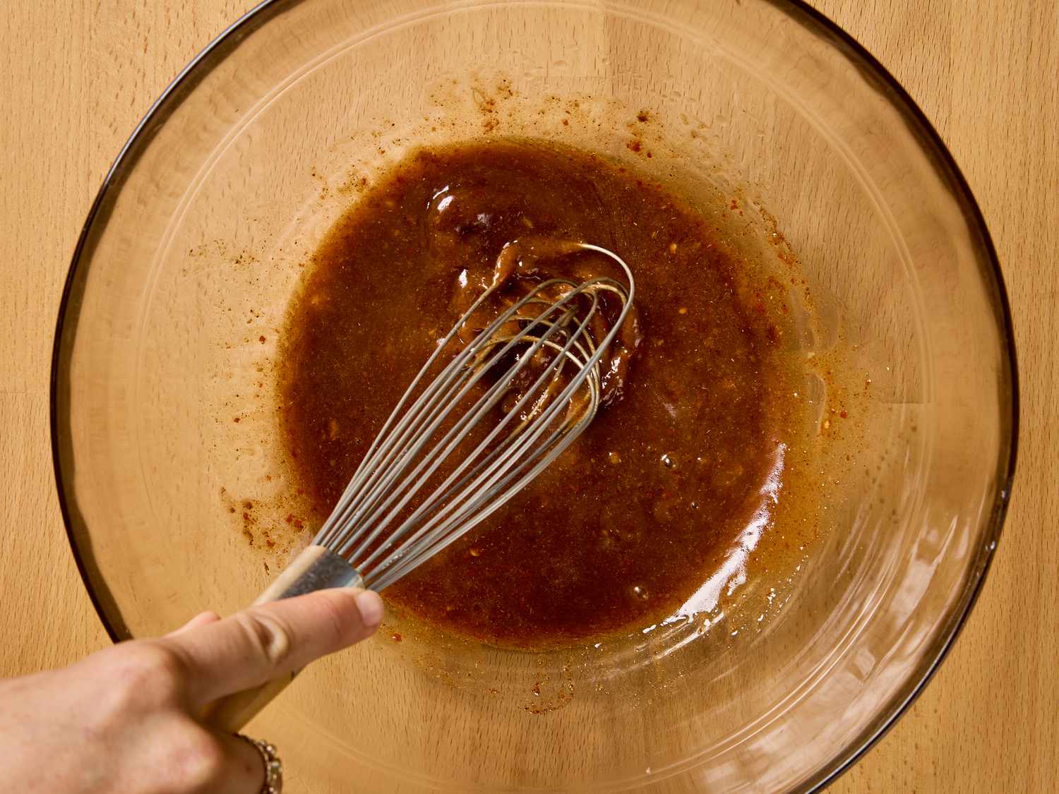 A hand whisking sauce in a large glass bowl