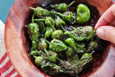 A small wooden bowl of grilled Padrón peppers sprinkled with salt. 
