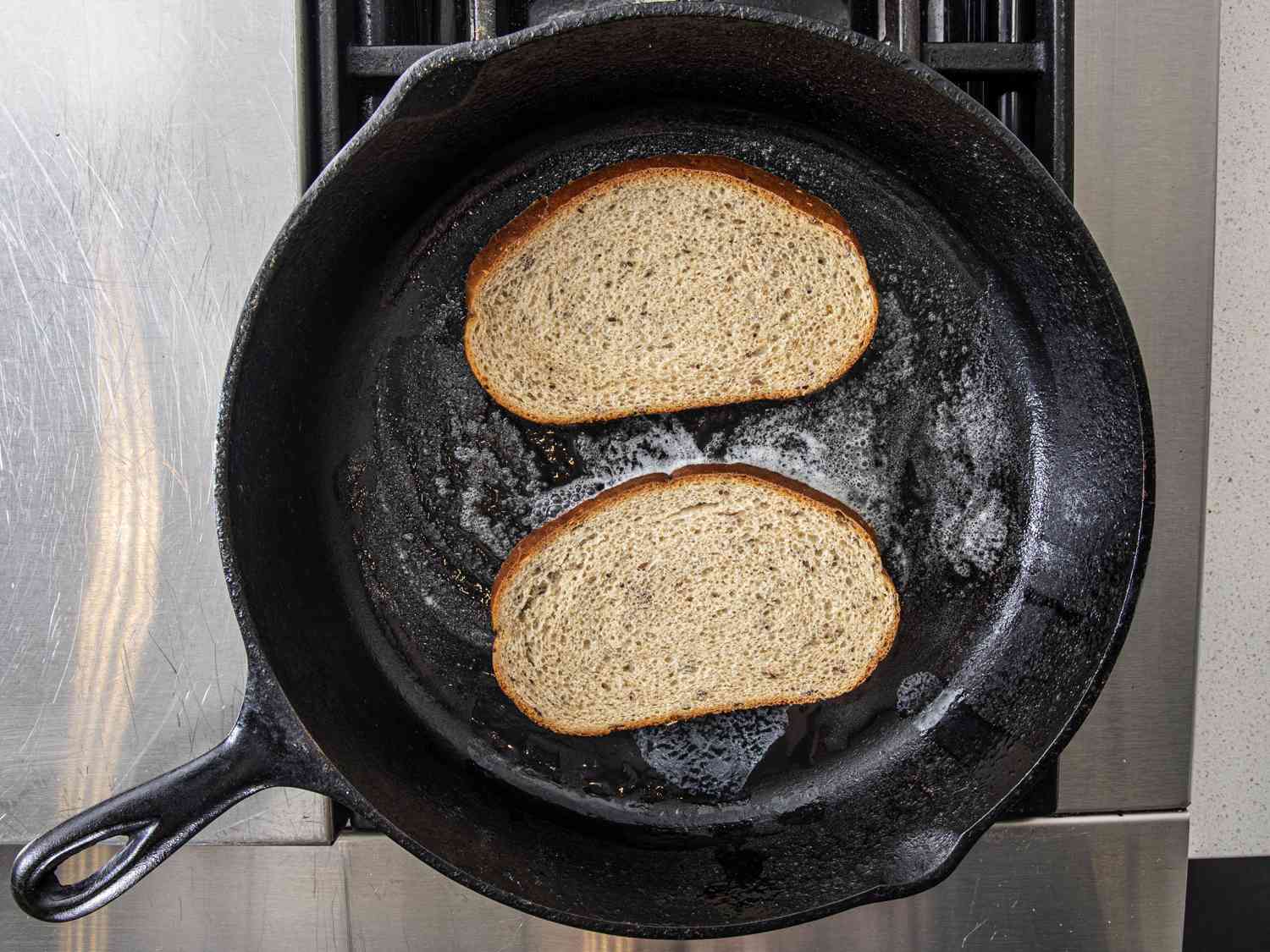 Bread toasting in butter in a pan.