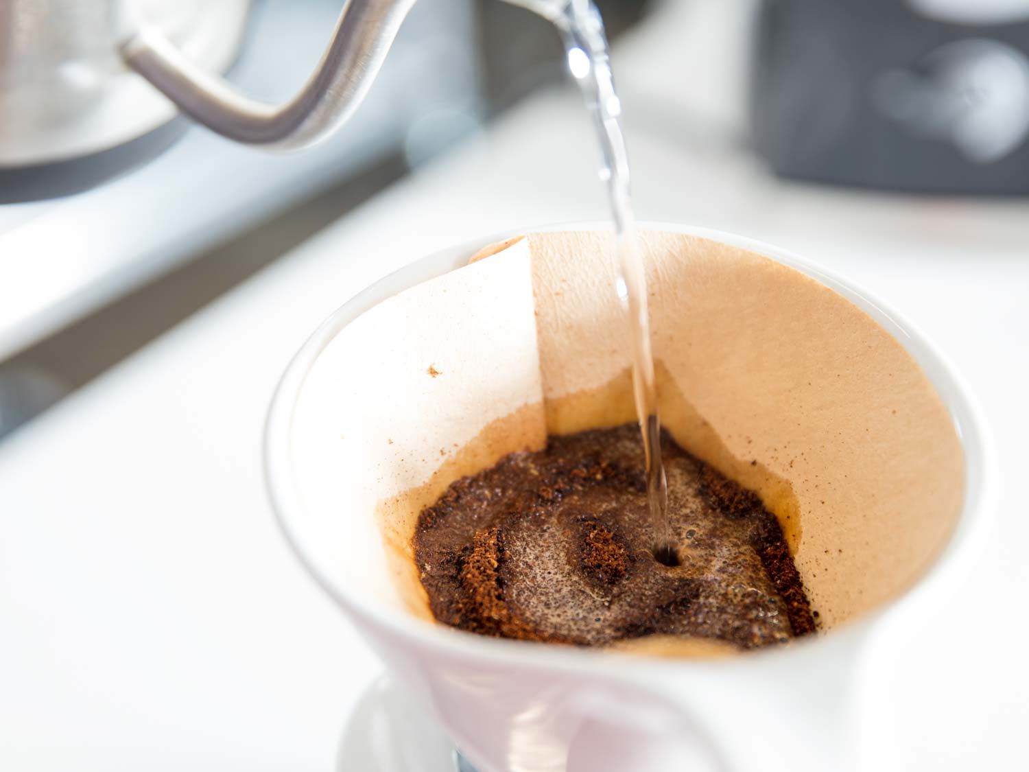 A goose-neck kettle is used to precisely wet coffee grounds, or "bloom" them, before brewing.