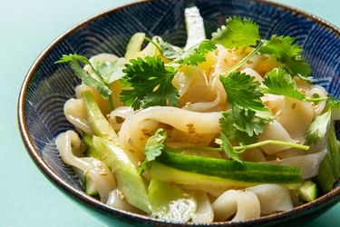 Bowl of cold sesame noodles topped with cucumber, celery, and cilantro