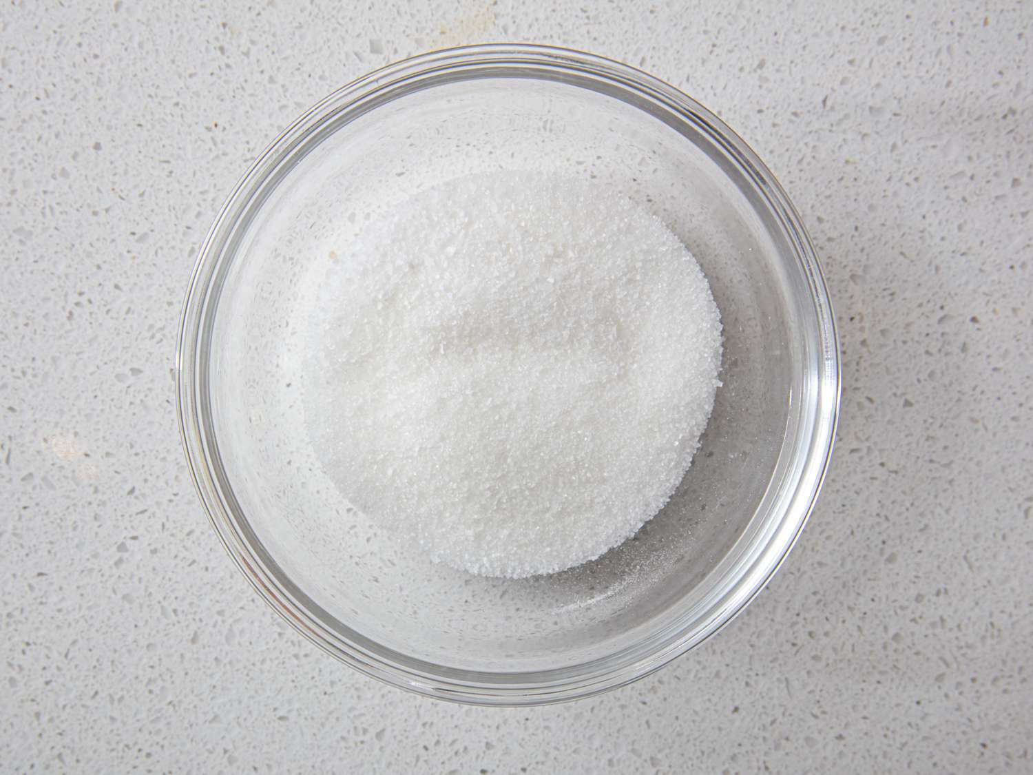 A glass bowl with sugar and salt on a white counter