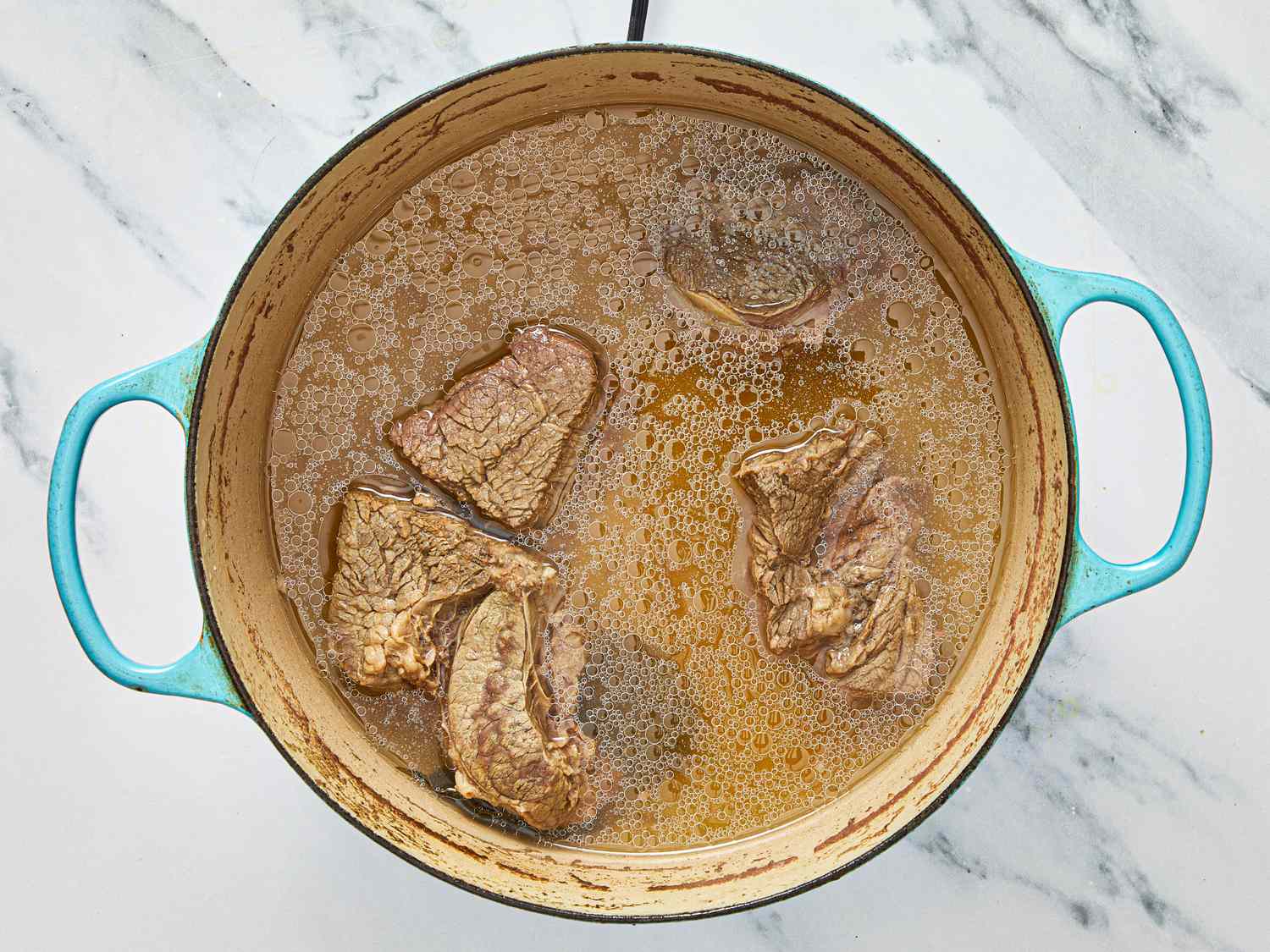 Large pot with pieces of meat simmering in liquid on a marble surface