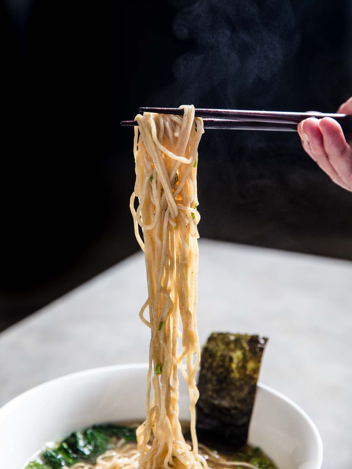 Chopsticks lifting a tangle of noodles from a bowl of shoyu ramen