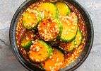 A bowl of marinated cucumber slices topped with sesame seeds and red chili flakes