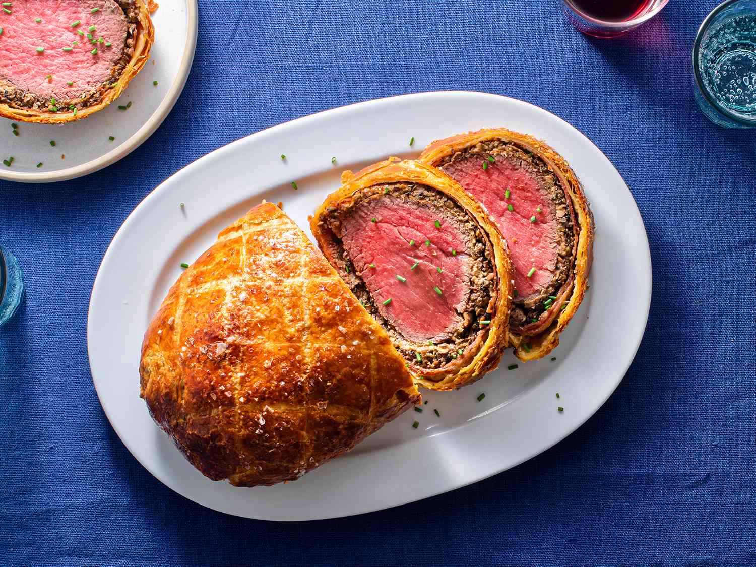 Beef Wellington on an oval white ceramic plate, with two slices of Wellington on the right hand side of the plate.