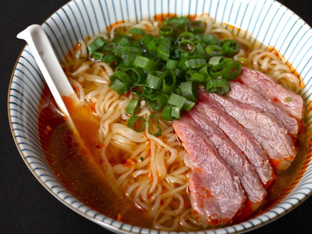 A bowl of ramen topped with scallions and thinly sliced flank steak.