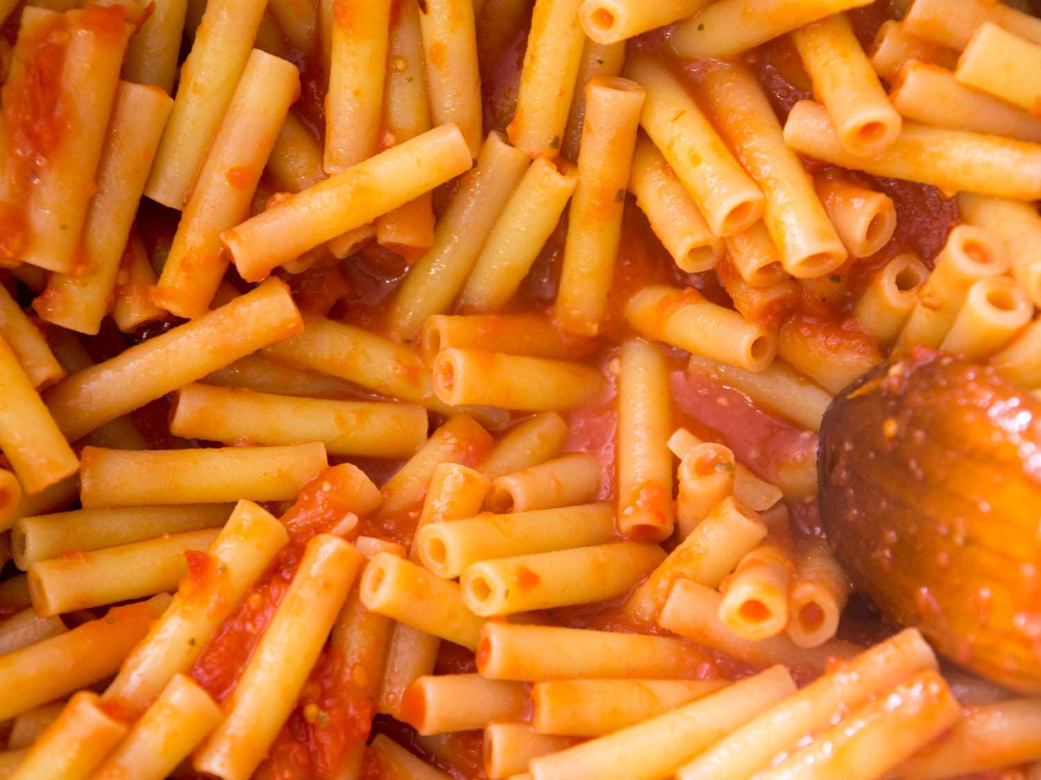 Close up view of cooked ziti being coated in tomato sauce.