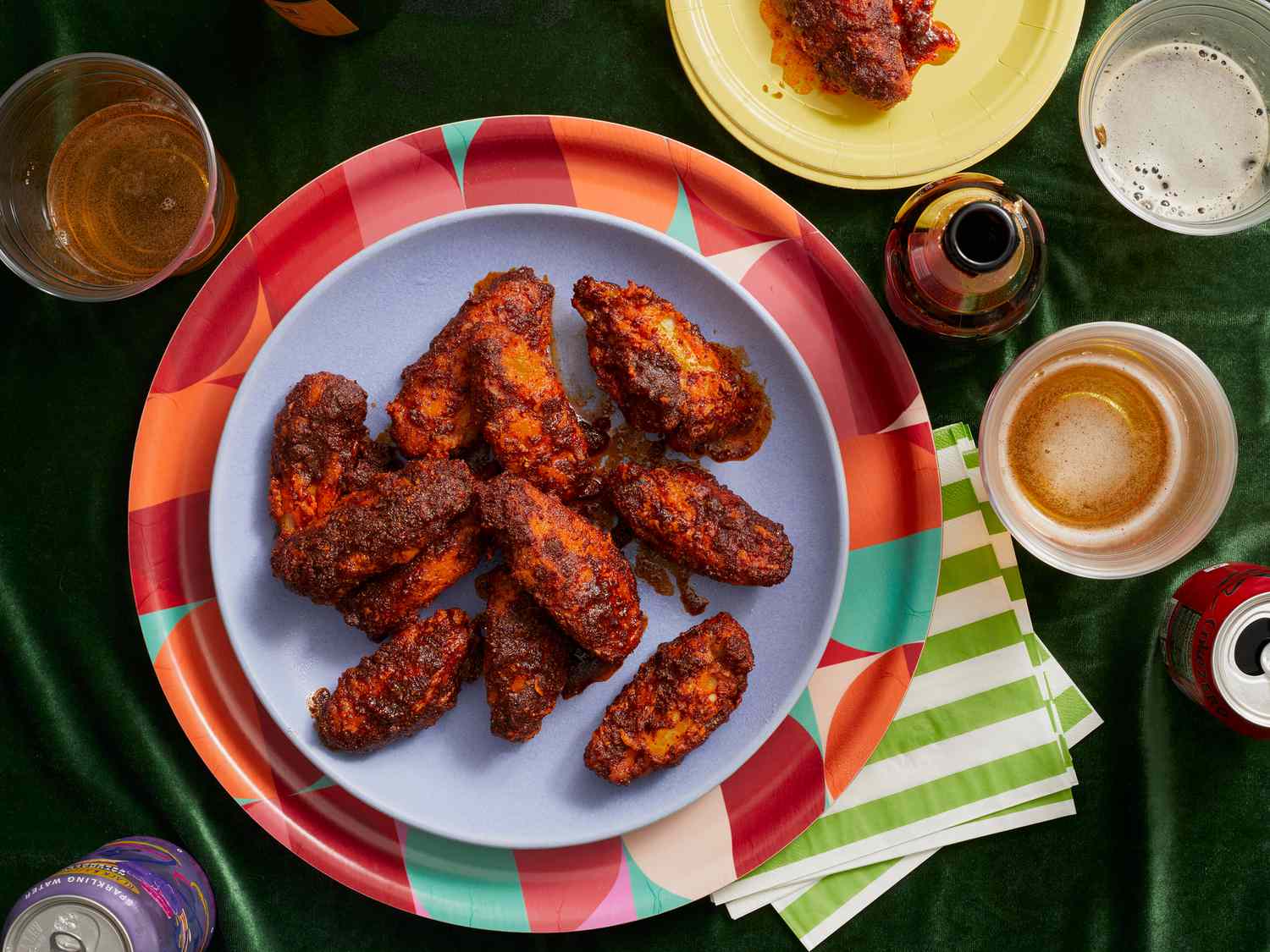 overhead of Wings on game day. Blue plate of spicy chicken wings on a colorful platter, beers, sodas and green tabletop