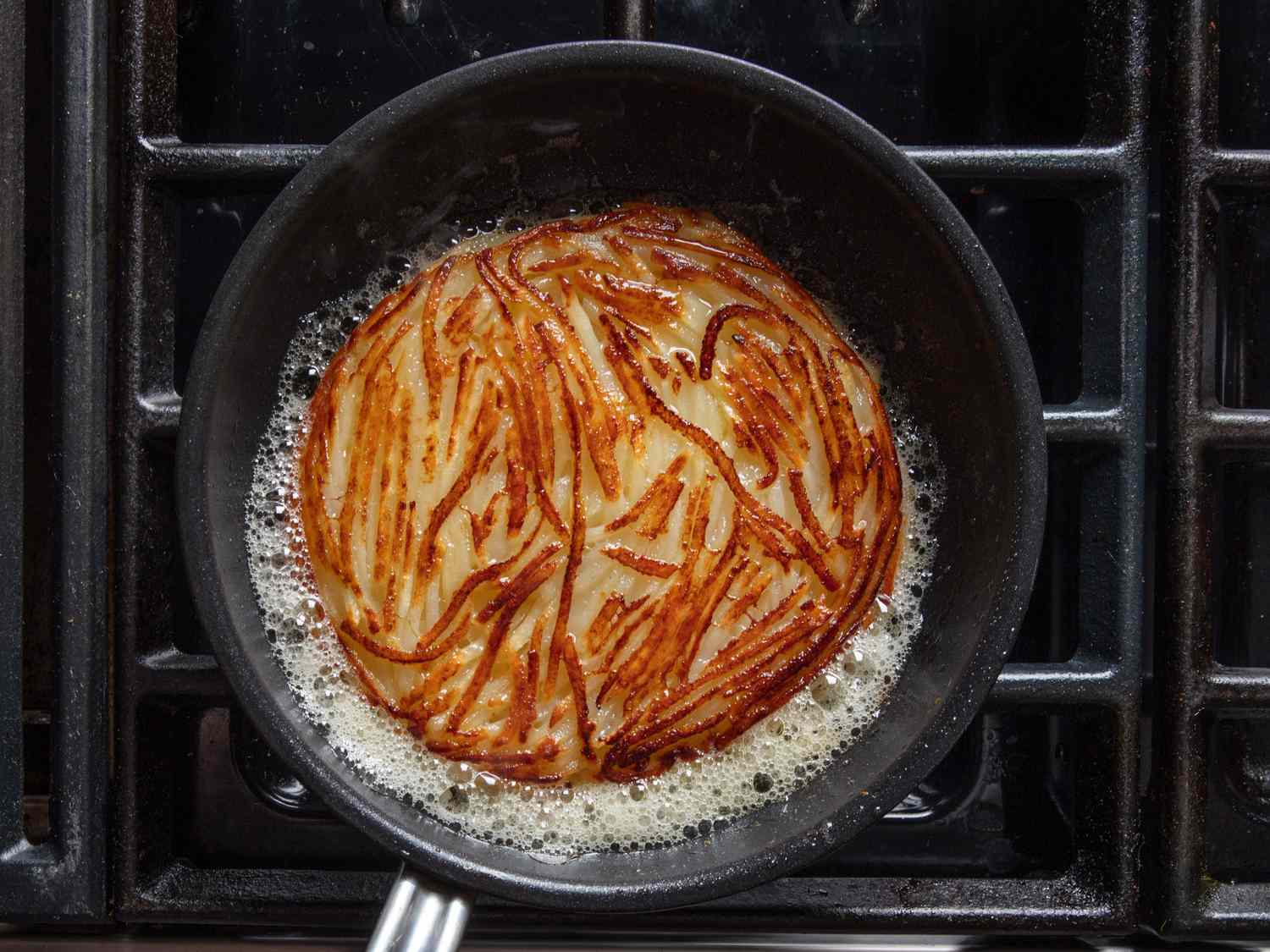 Pommes Darphin in a skillet, the hot butter foaming around the sides. It's well browned and crispy on top.