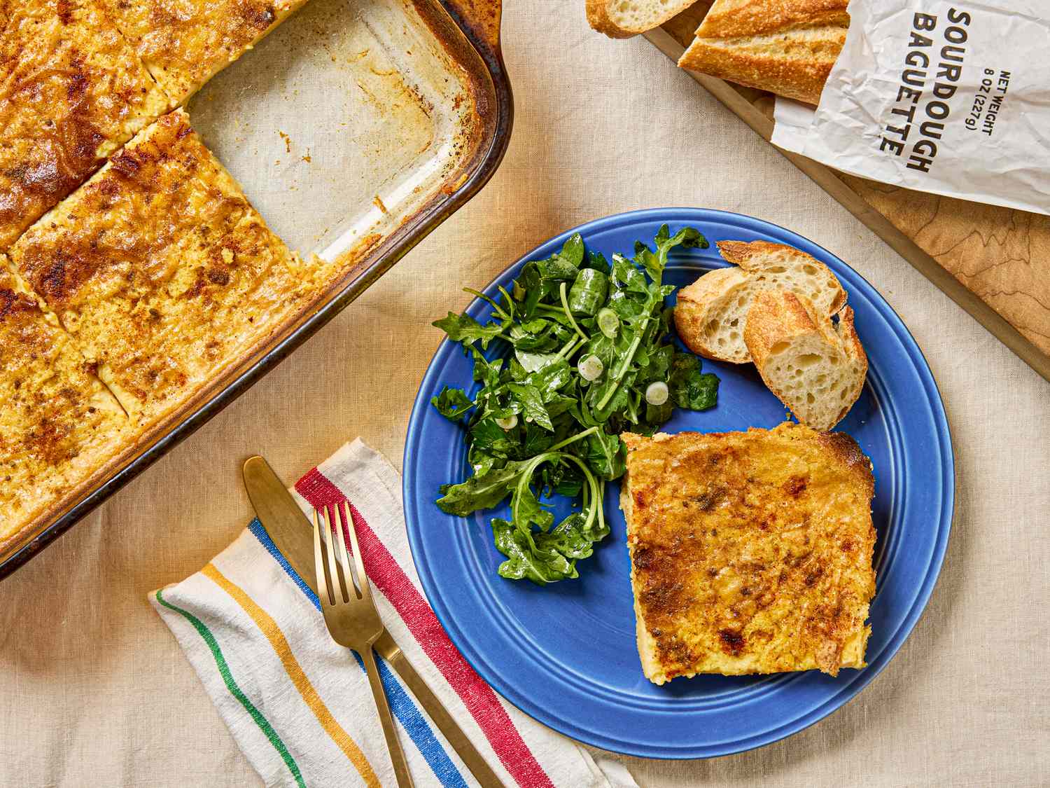 Plate with a slice of casserole arugula salad and bread casserole dish and bread loaf in background