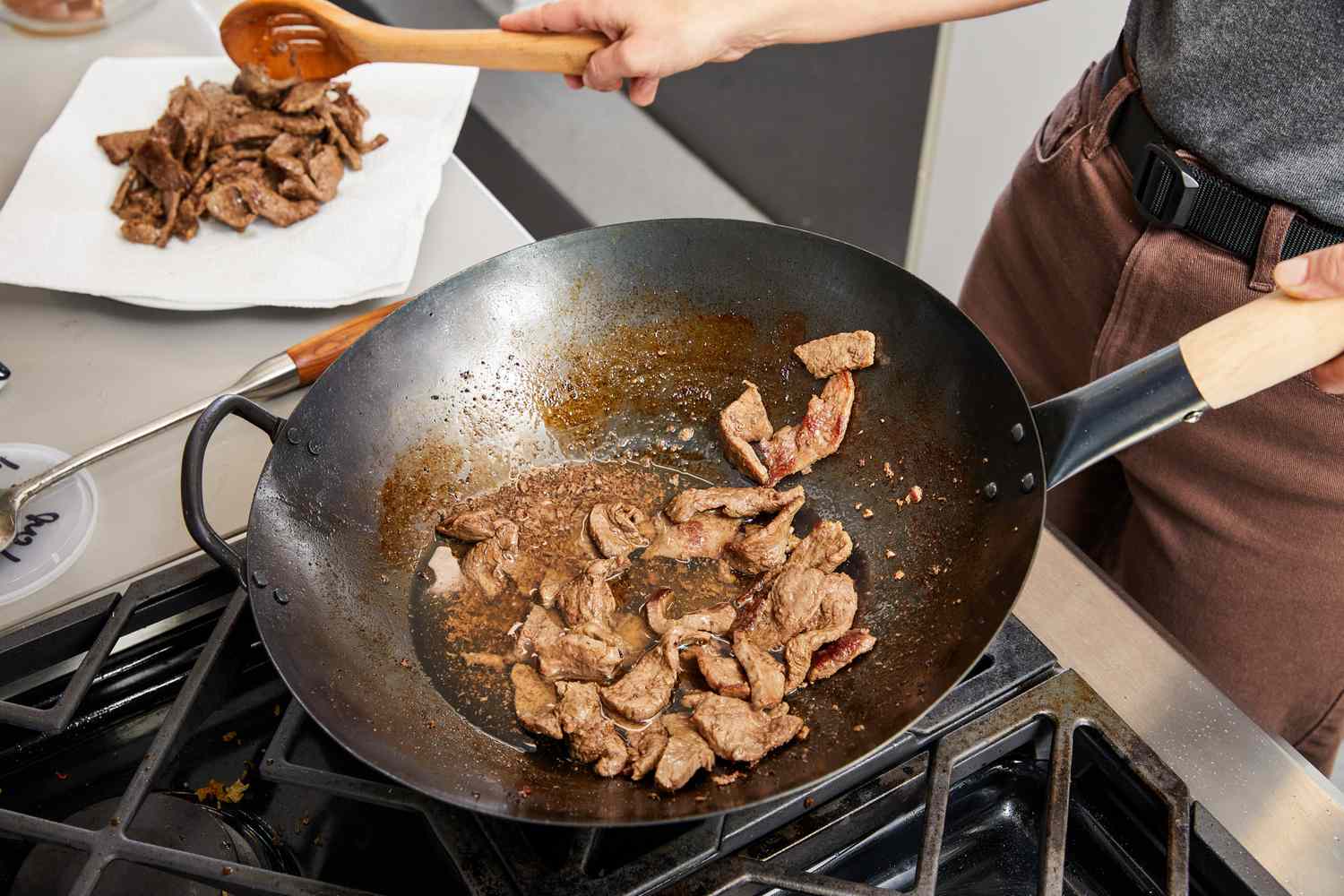 Person cooking in a Mammafong Pre-Seasoned Blue Carbon Steel Flat-Bottom Pow Wok