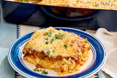 A serving of baked spaghetti on a plate garnished with herbs with a baking dish in the background