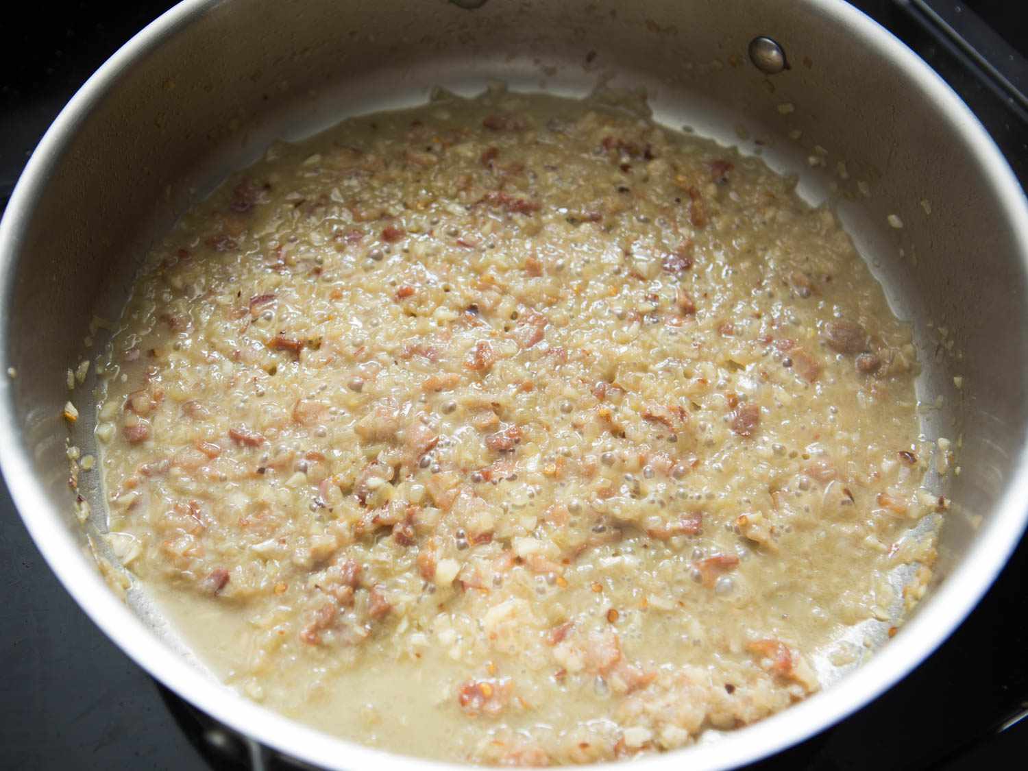 Evaporated wine and clam liquid and jammy shallot-bacon mixture on stainless steel pan