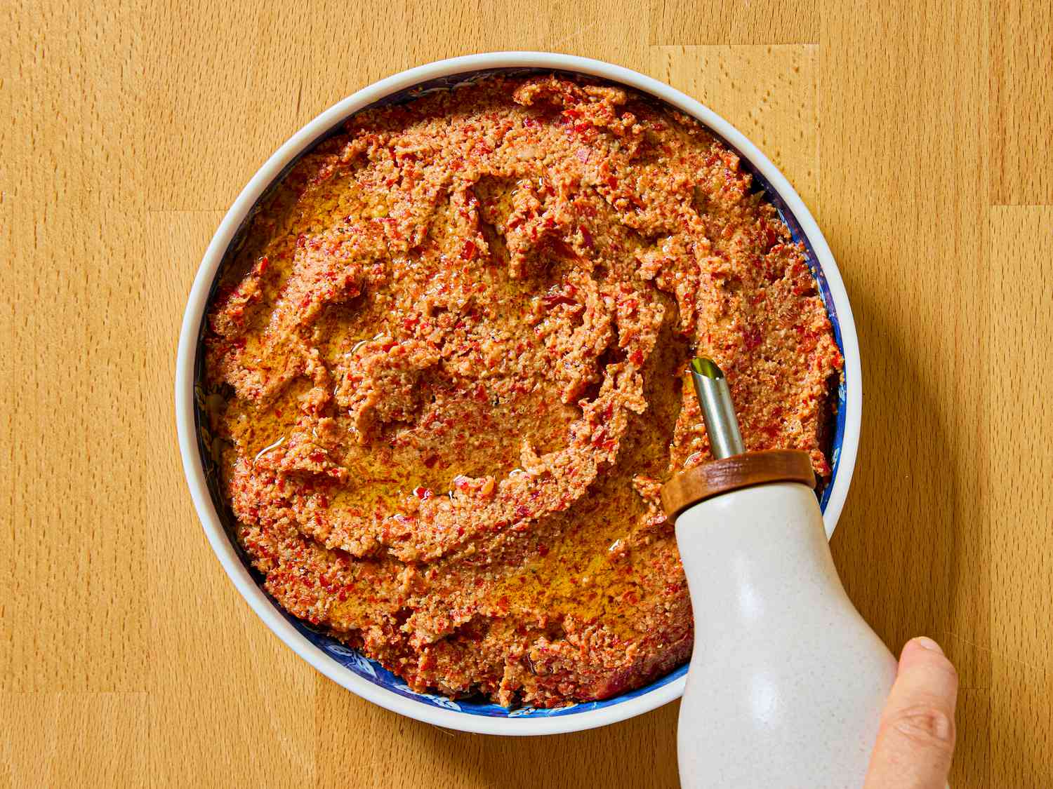 A bowl filled with muhammara topped with olive oil on a wooden surface