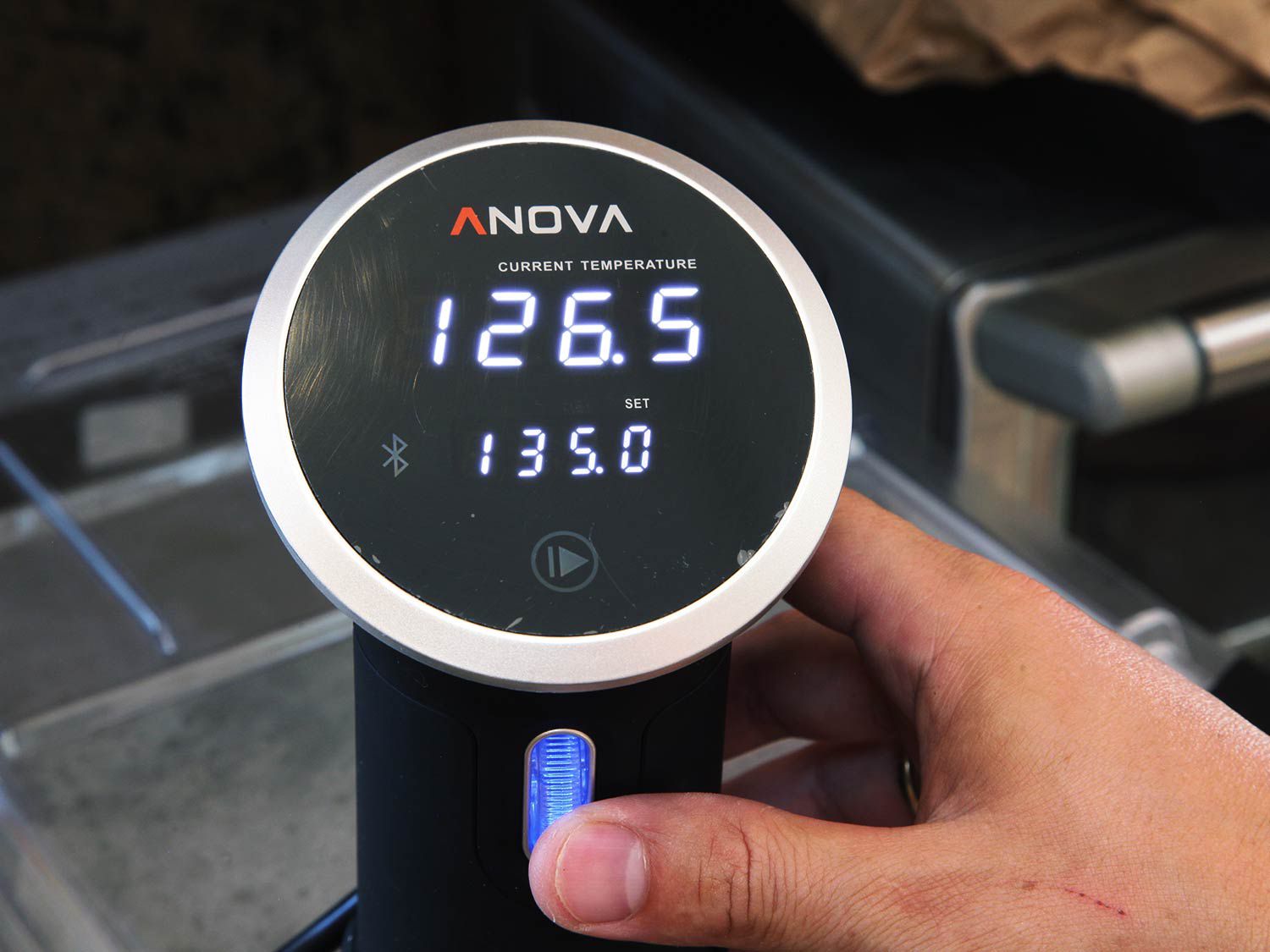 A hand adjusts the temperature setting on an immersion circulator.