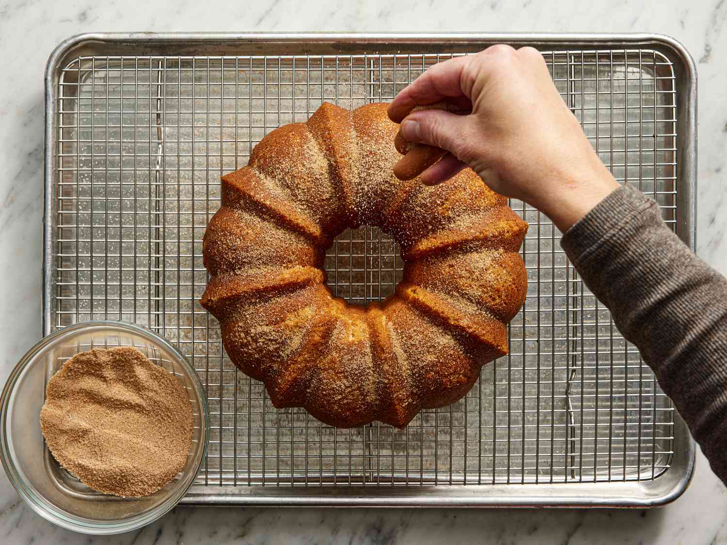 Overhead view of sprinkling sugar on cake resting on wire rack