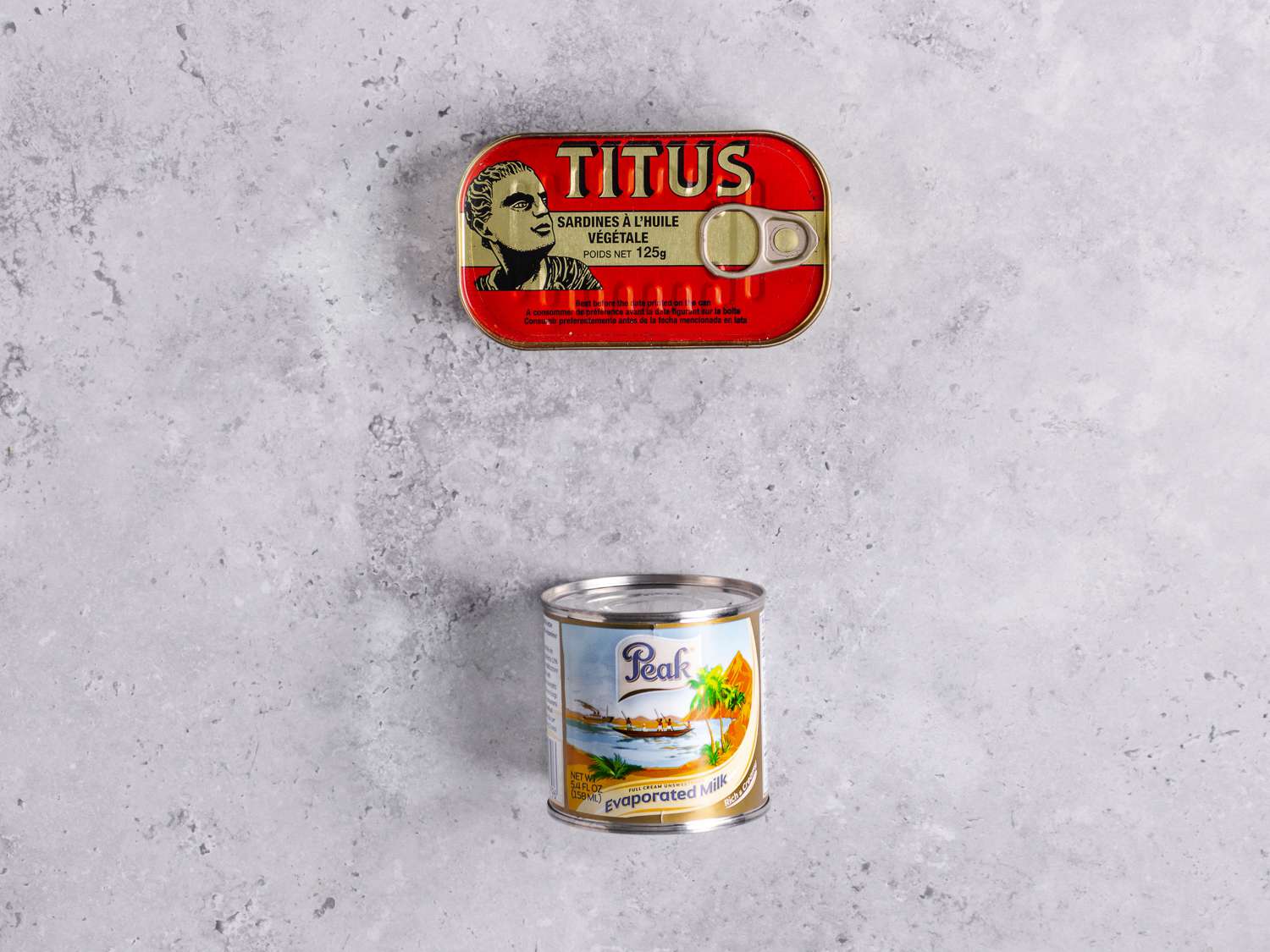 A package of tinned sardines and a can of evaporated milk on a marbled grey surface