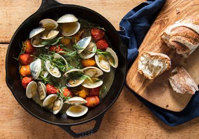 Broiled clams with tomatoes and tarragon in cast iron skillet beside wooden board with crusty bread