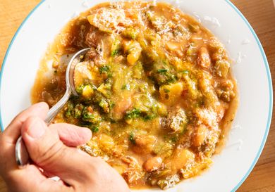 A hand holding a spoon over a bowl of hearty bean and vegetable stew