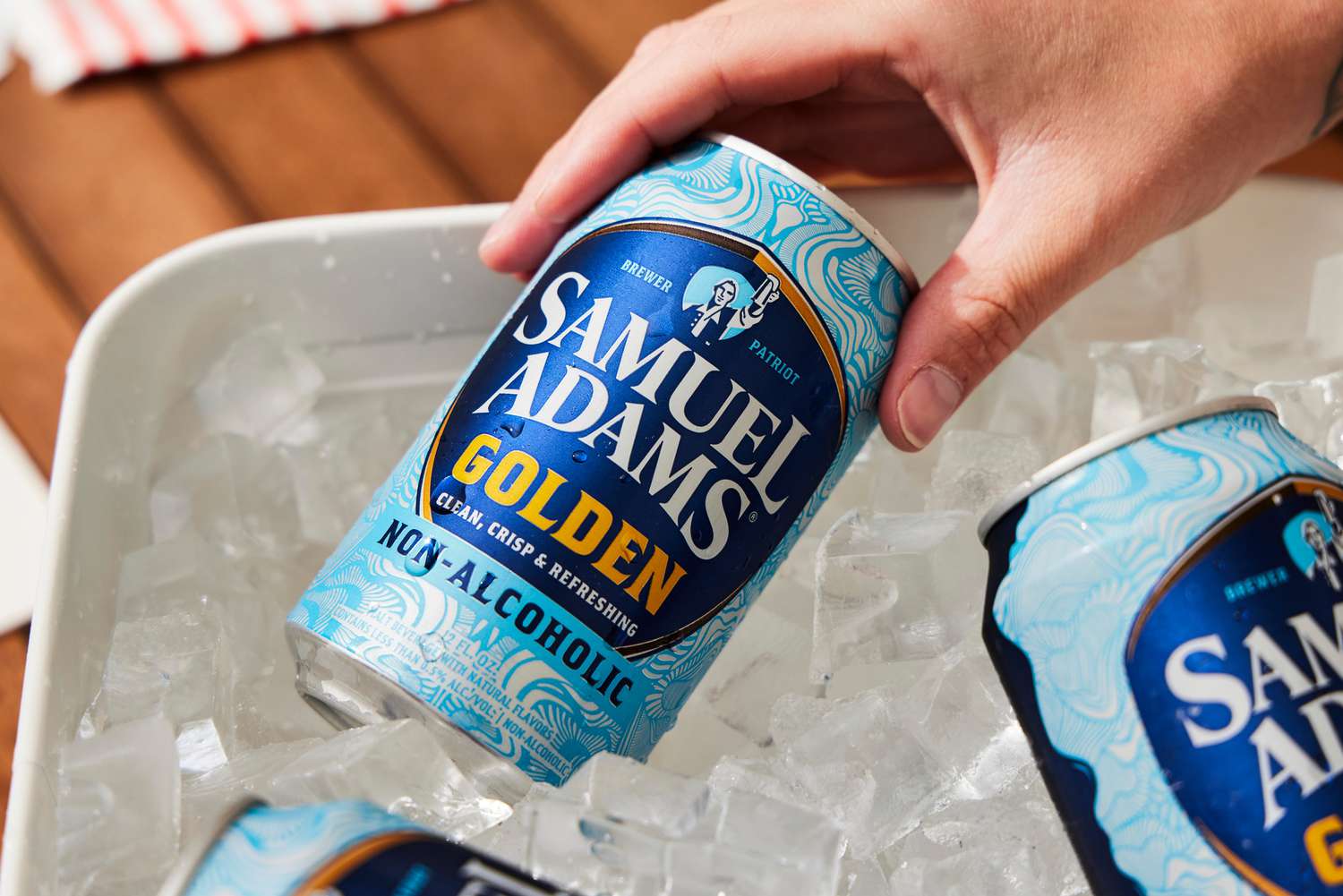  a hand taking a can of Sam Adams golden out of a bucket of ice