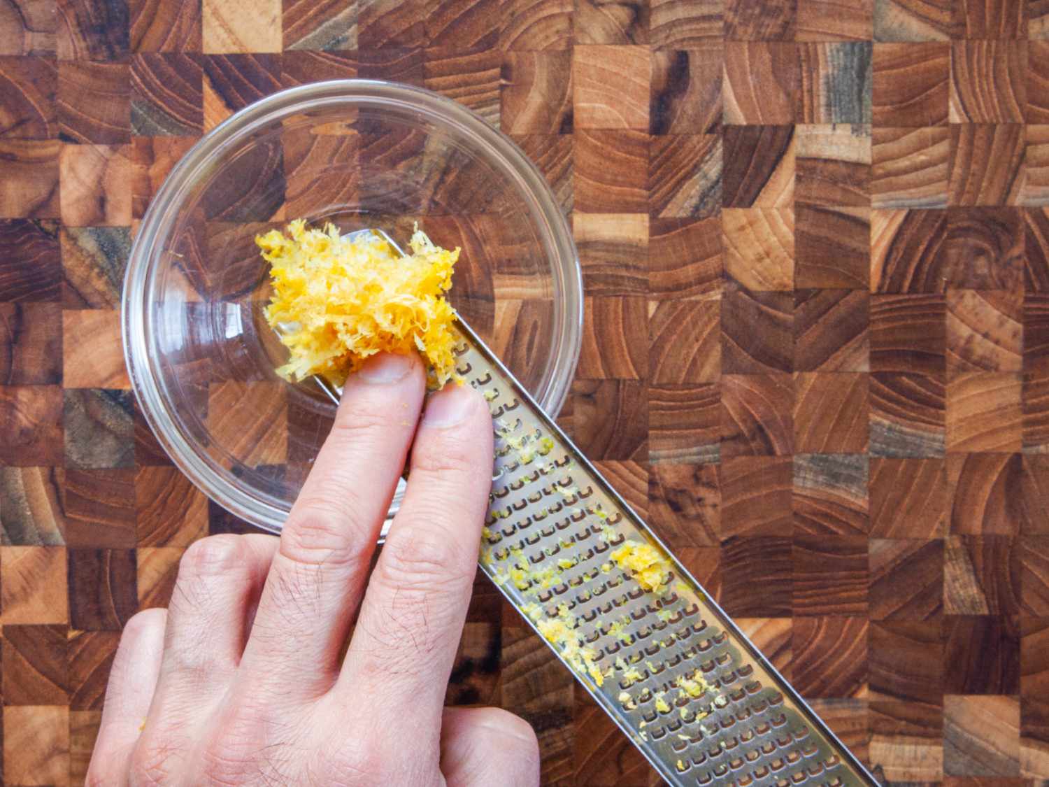 Two fingers removing lemon shavings from the Microplane Classic zester