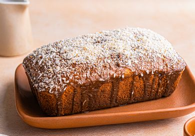 A loaf of banana coconut cake on a platter topped with shredded coconut