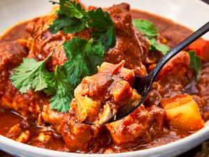 Closeup of Pollo Guisado served in a bowl with a spoon lifting a bite garnished with cilantro