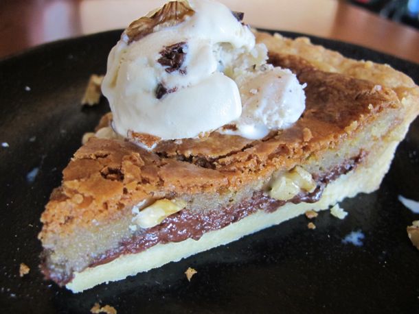 A slice of chocolate chip cookie tart, topped with a scoop of ice cream.