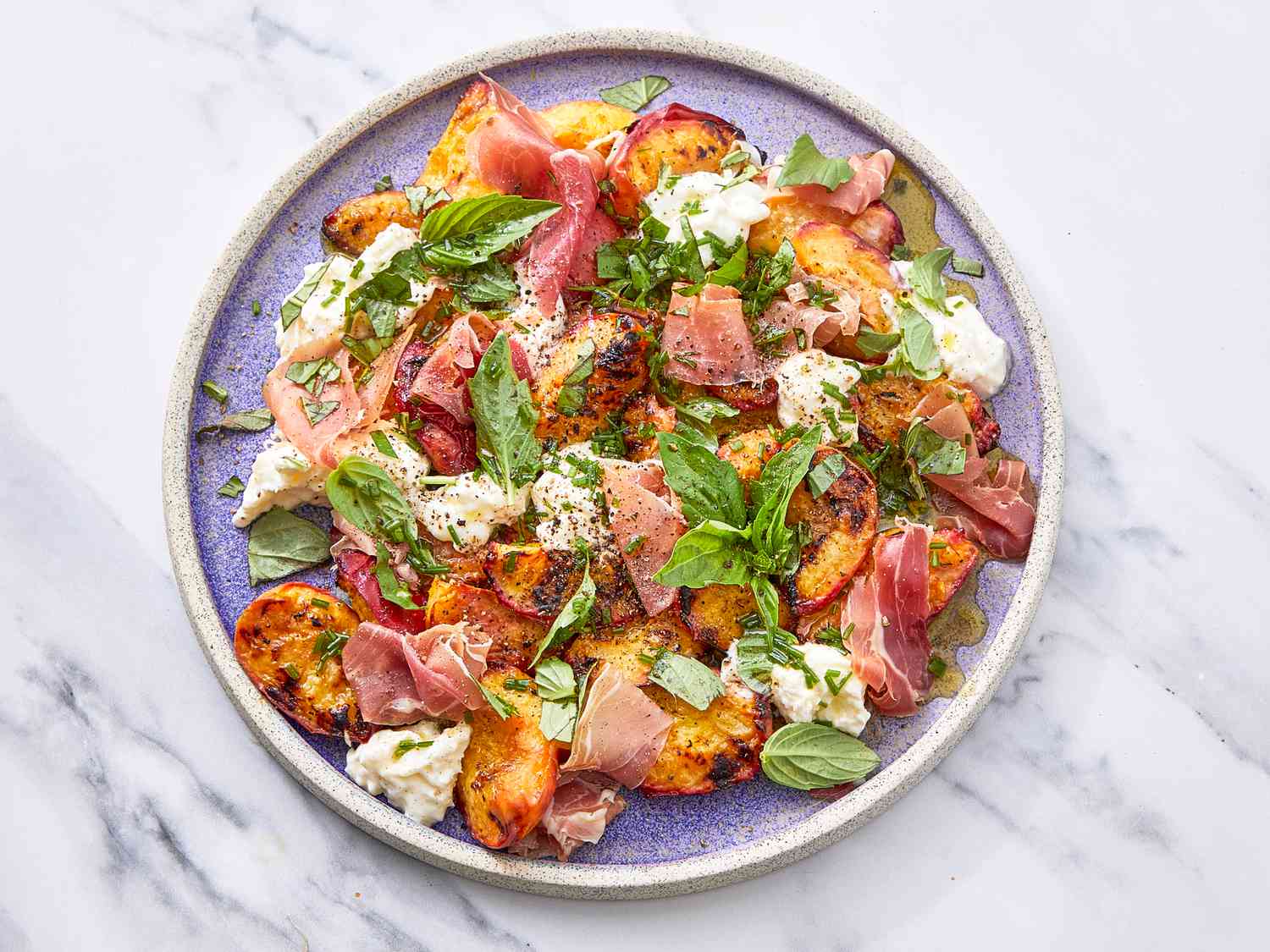 A plate of grilled peach salad with herbs, prosciutto, and cheese