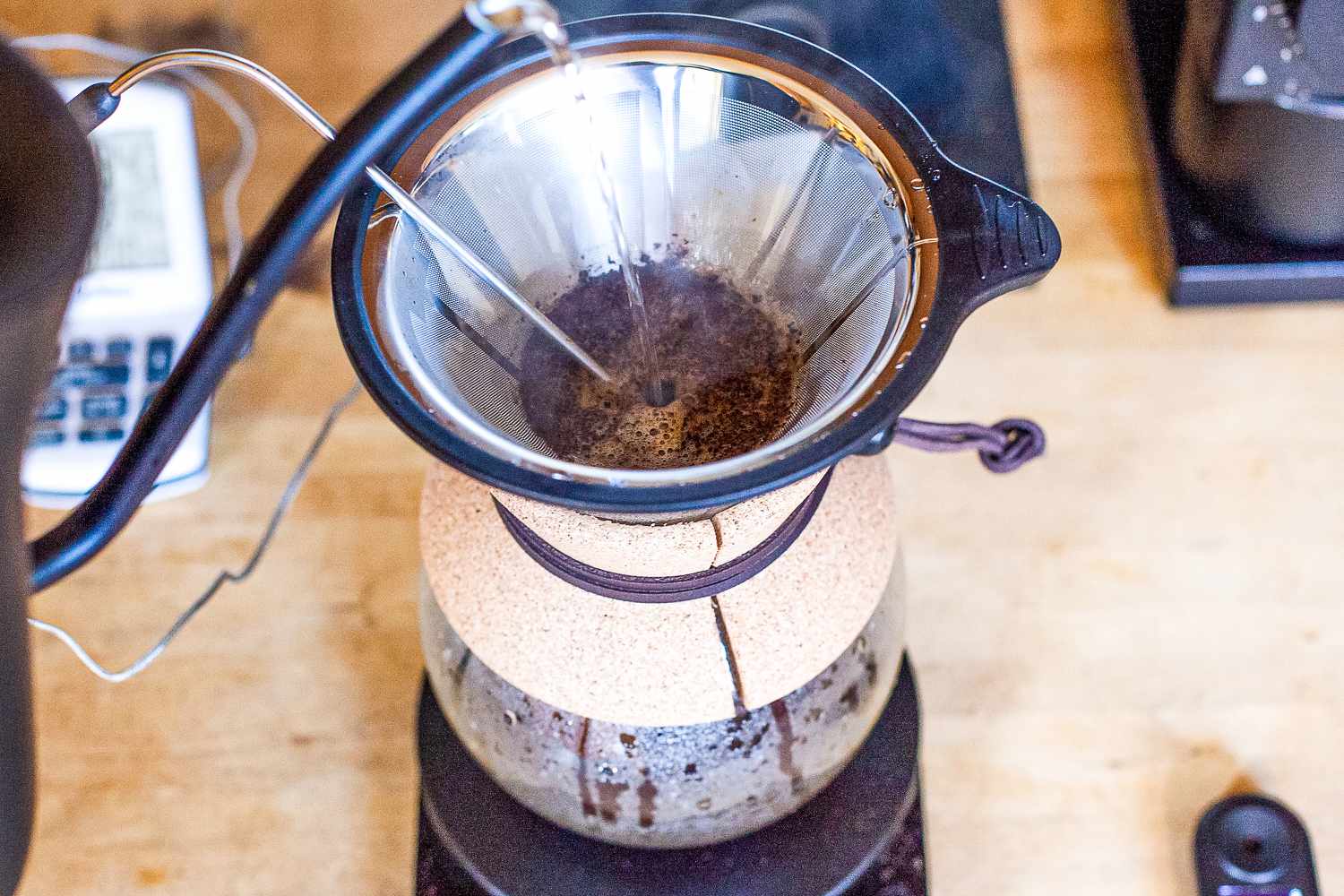 Pour-over coffee brewing with filter and carafe and water being added from a gooseneck kettle.