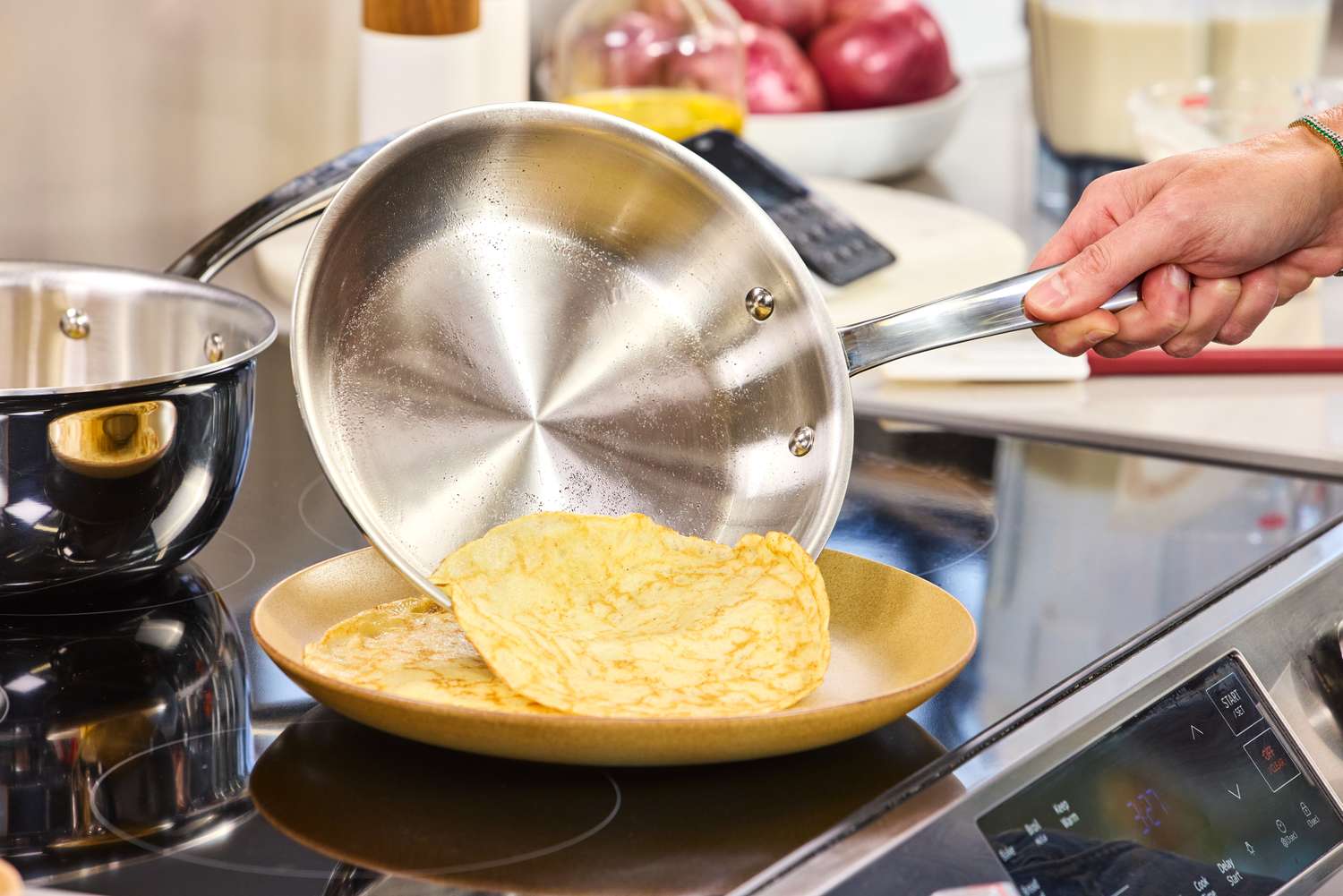 A person cooks a crepe in the All-Clad G5 Graphite Core Stainless Steel 10 Piece Cookware Set pan