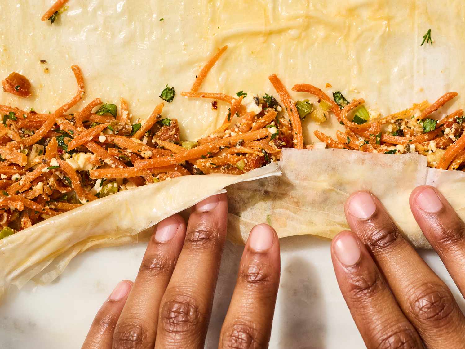 Hands rolling pastry dough filled with shredded carrot mixture
