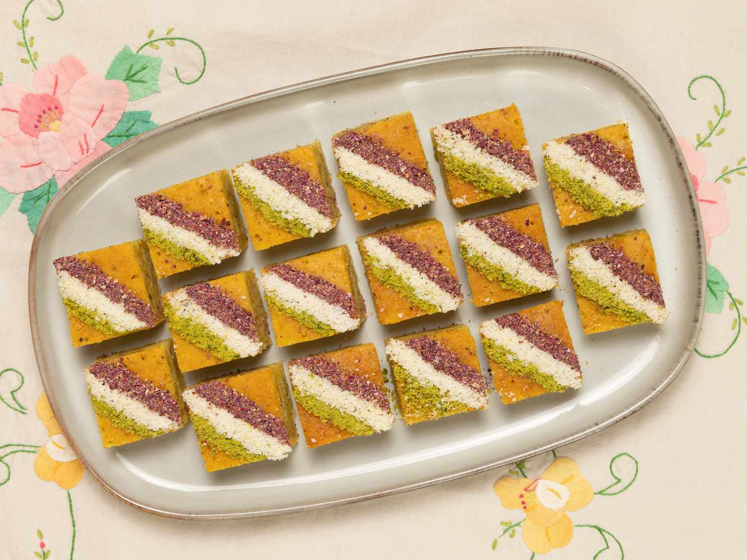 Baklava squares lined up on a white platter, on a floral and white fabric