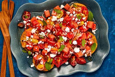 A dark bowl with tomato-watermelon salad, sprinkled with mint and feta, 