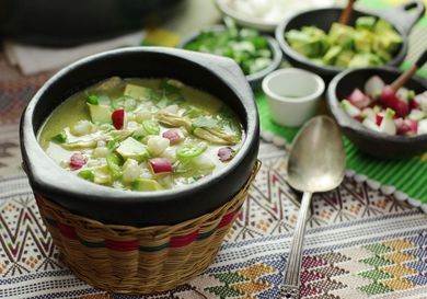 A bowl of green pozole verde topped with avocado and radish.