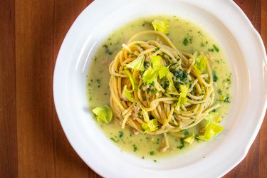 Overhead closeup of spaghetti with canned-clam sauce, served on a deep, white plate and garnished with tender celery leaves.