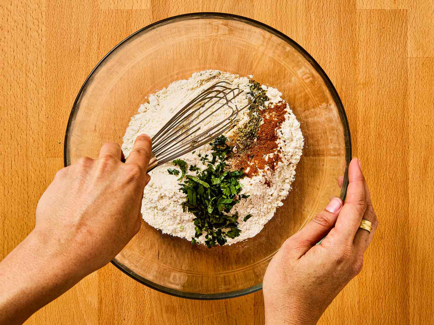 whisking together flour, sazón spice blend, pepper, garlic powder, sofrito, and culantro or cilantro leaves in a large bow